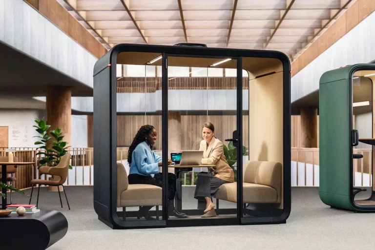 Dos personas reunidas dentro de una cabina acústica en una oficina diáfana