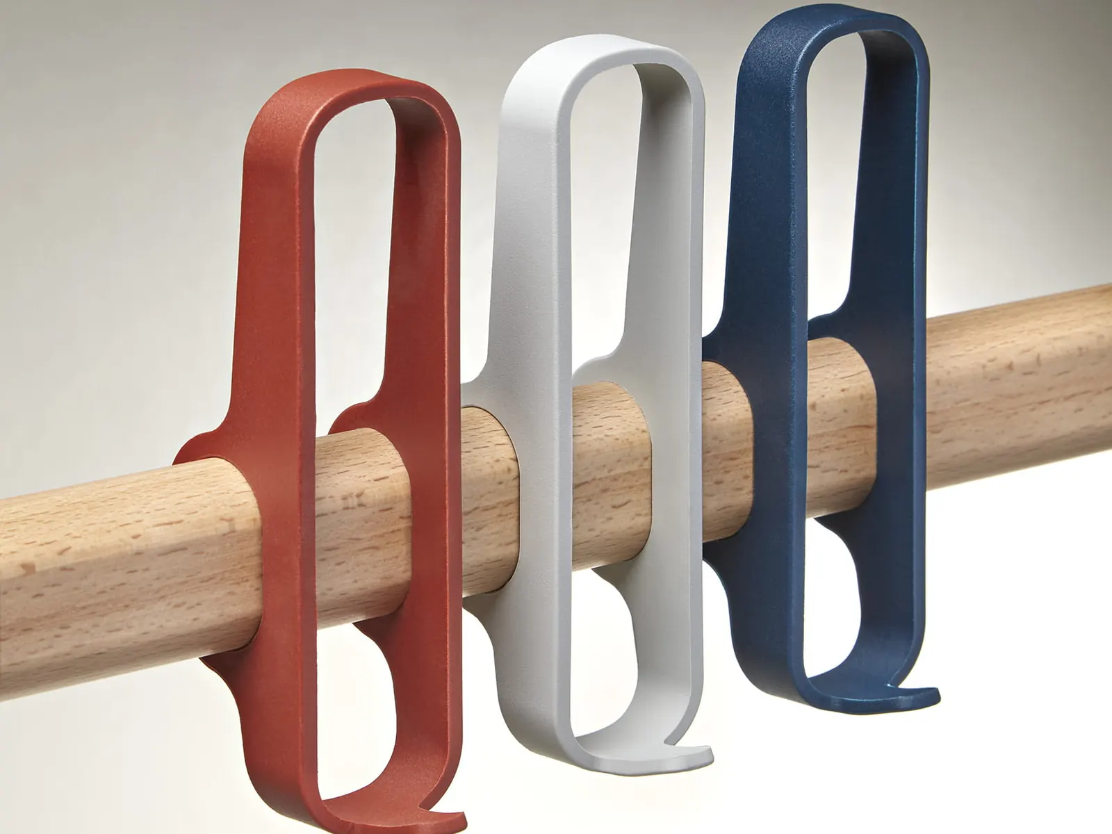 Detalle de tres perchas de Made Design Milard en rojo, gris y azul sobre el listón de madera